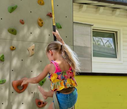 Bambina che scala la parete da arrampicata nell’area giochi esterna del kids club di un family hotel in Alto Adige
